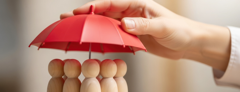 Fünf Holzfiguren stehen unter einem roten Schirm, der von einer Hand gehalten wird